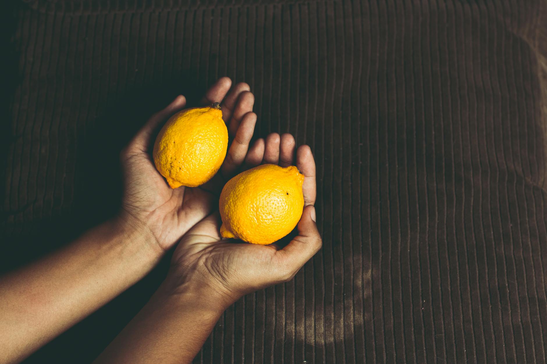 Hand holding a fresh lemon against bright yellow background, symbolizing natural clitoral health and vitality
