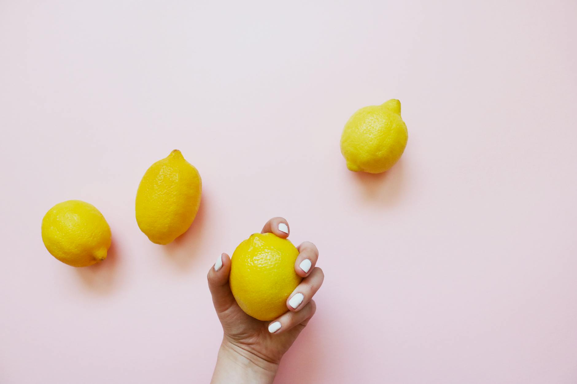 Hand holding a fresh lemon on a soft pink background surrounded by additional lemons, symbolizing fresh approaches to intimate conversations