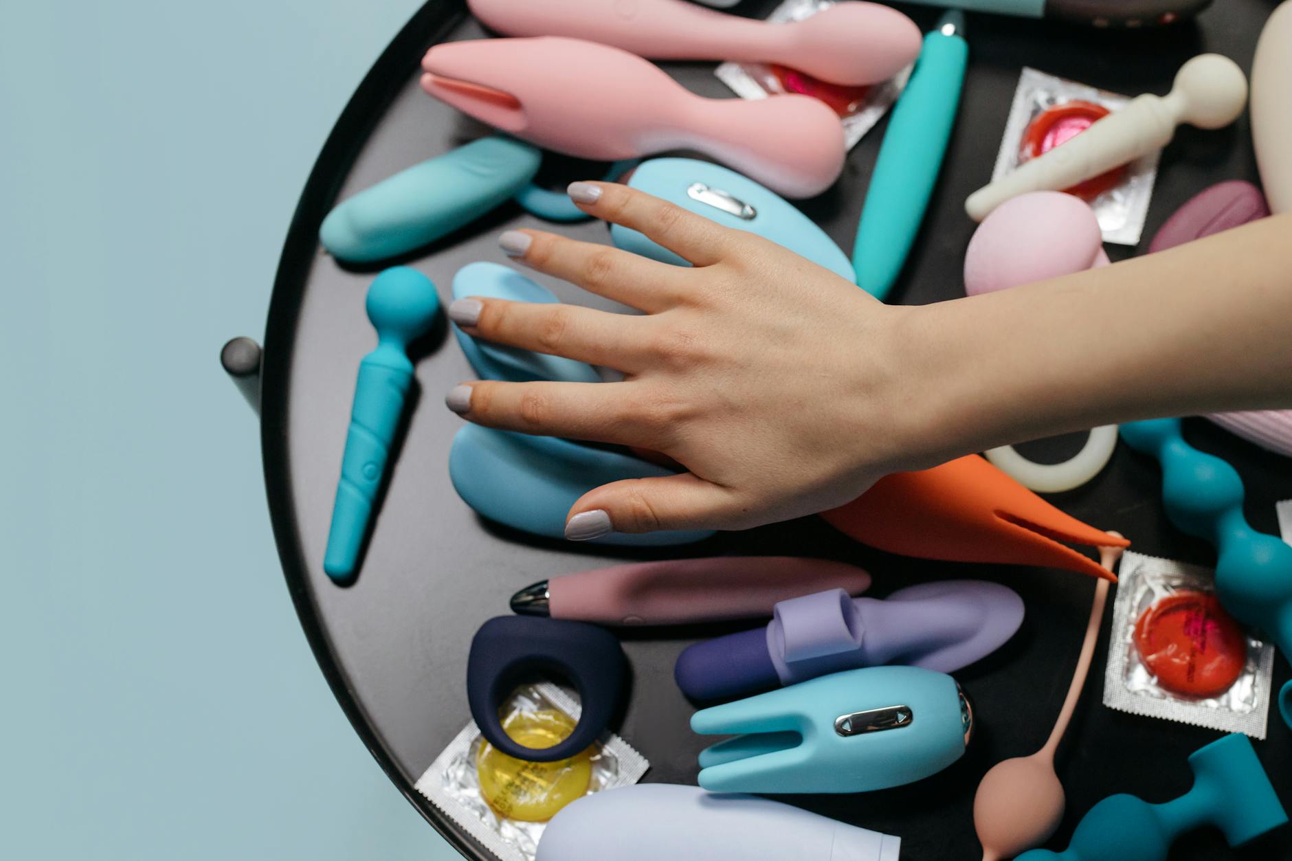A hand reaching over a collection of colorful vibrators, symbolizing choice and personal control in intimacy.
