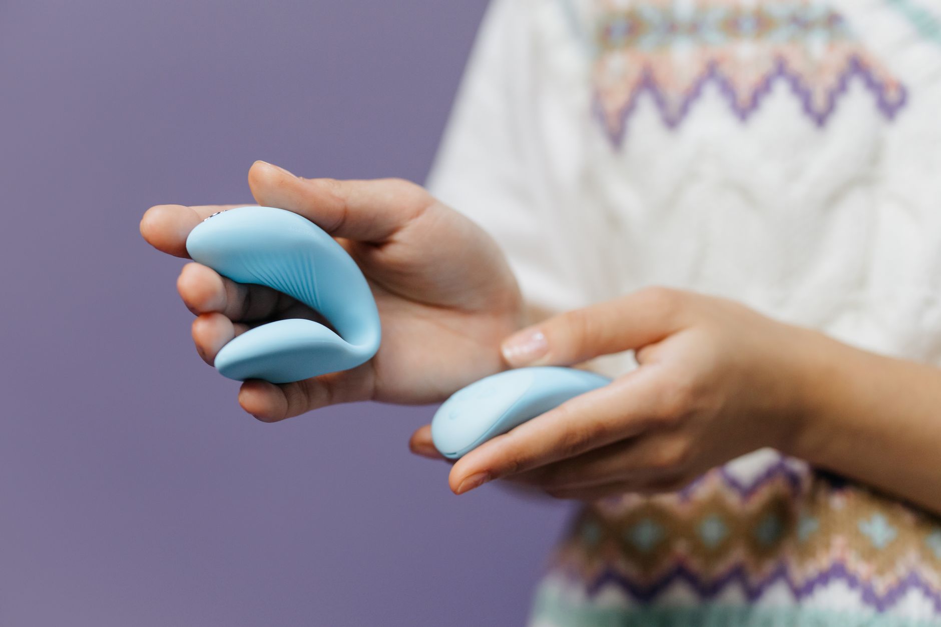 Close-up of hands holding a sleek blue vibrator together, showing intimate exploration and partnership.