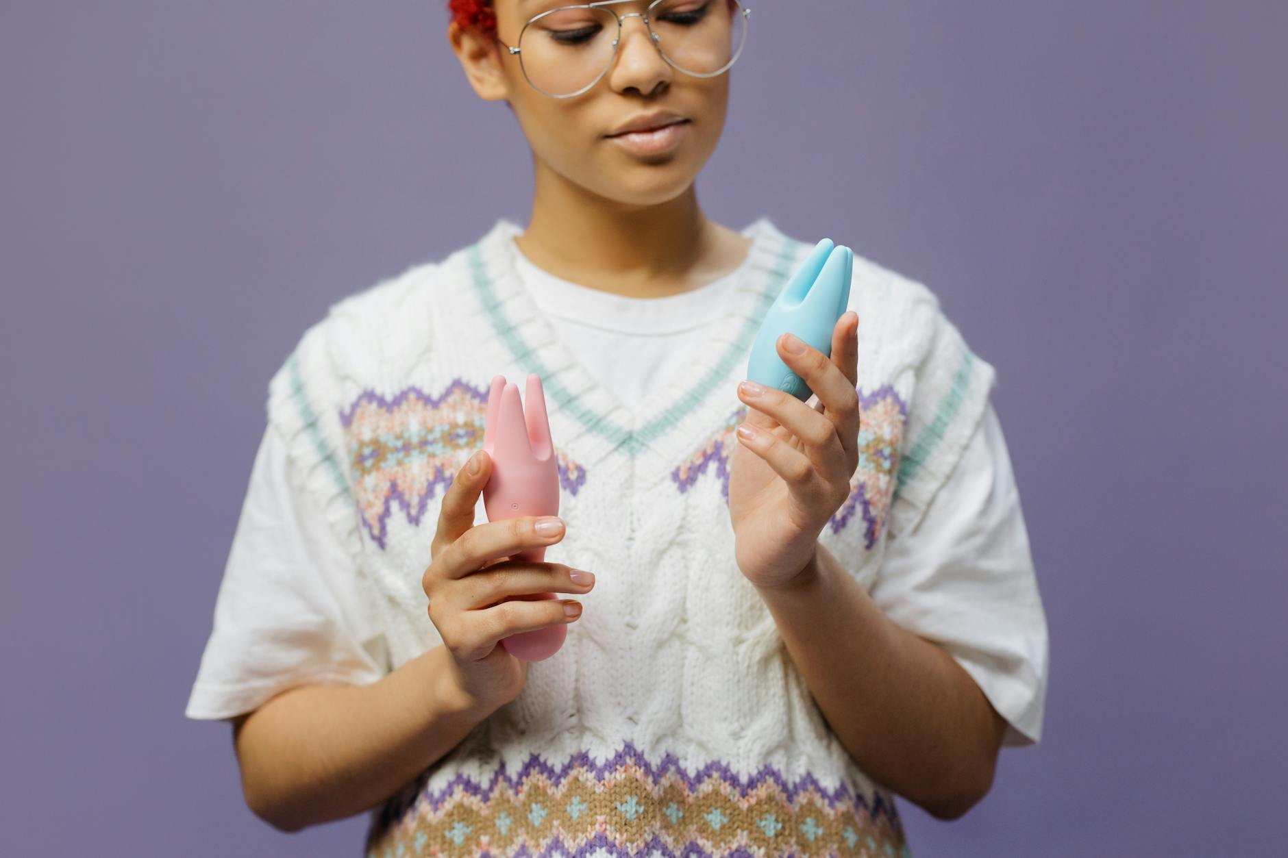Woman holding blue and pink silicone vibrators with thoughtful expression
