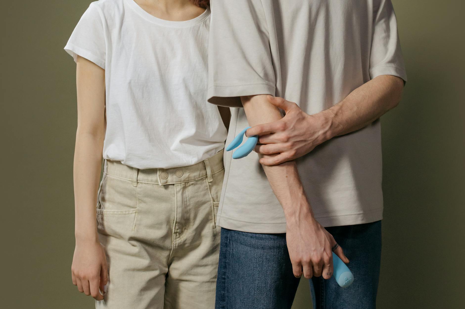 Ein Paar steht zusammen drinnen und hält einen blauen Vibrator, was moderne Intimität symbolisiert.